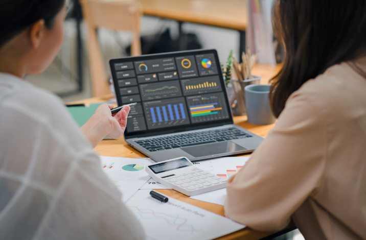 Zwei Frauen sitzen vor einem Laptop und schauen auf einen Bildschirm mit Grafiken 