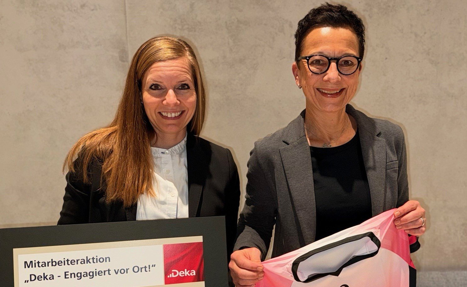 Zwei Frauen halten eingerahmten Spendenscheck und Laufshirts in die Kamera